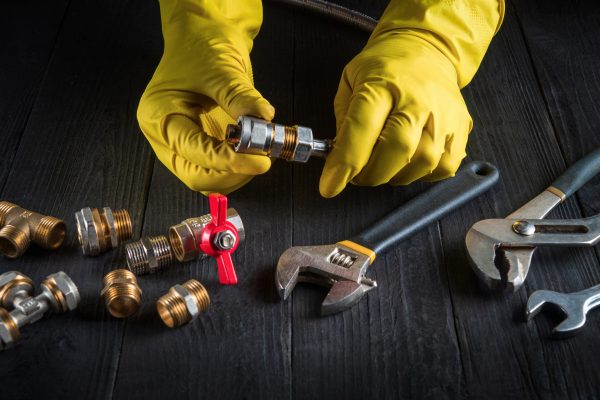 Professional plumber connects brass fittings to plumbing hose. Close-up of hand of the master during work in workshop